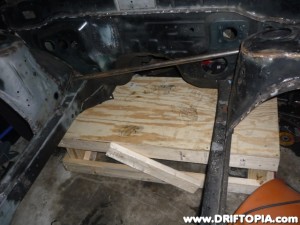 The bare 240sx chassis has been raised on two wooden platforms to prepare for the replacement of the crimped frame rails.