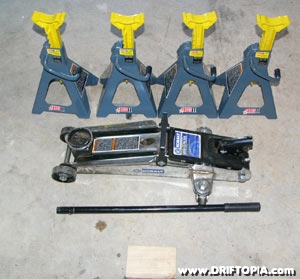A picture of the tools required to place a car on jack stands.  4 - jack stands, 1 hydraulic jack and a wood block