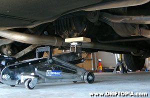 The rear end of a 240sx being lifted by a hydraulic jack at the rear diff.